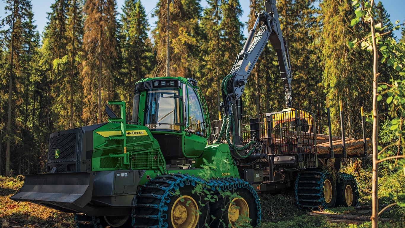 A 2010 H-Series Forwarder moving felled logs into a trailer in the forest.
