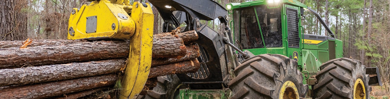 Green logging grapple skidder transporting logs in a forest during timber harvesting.