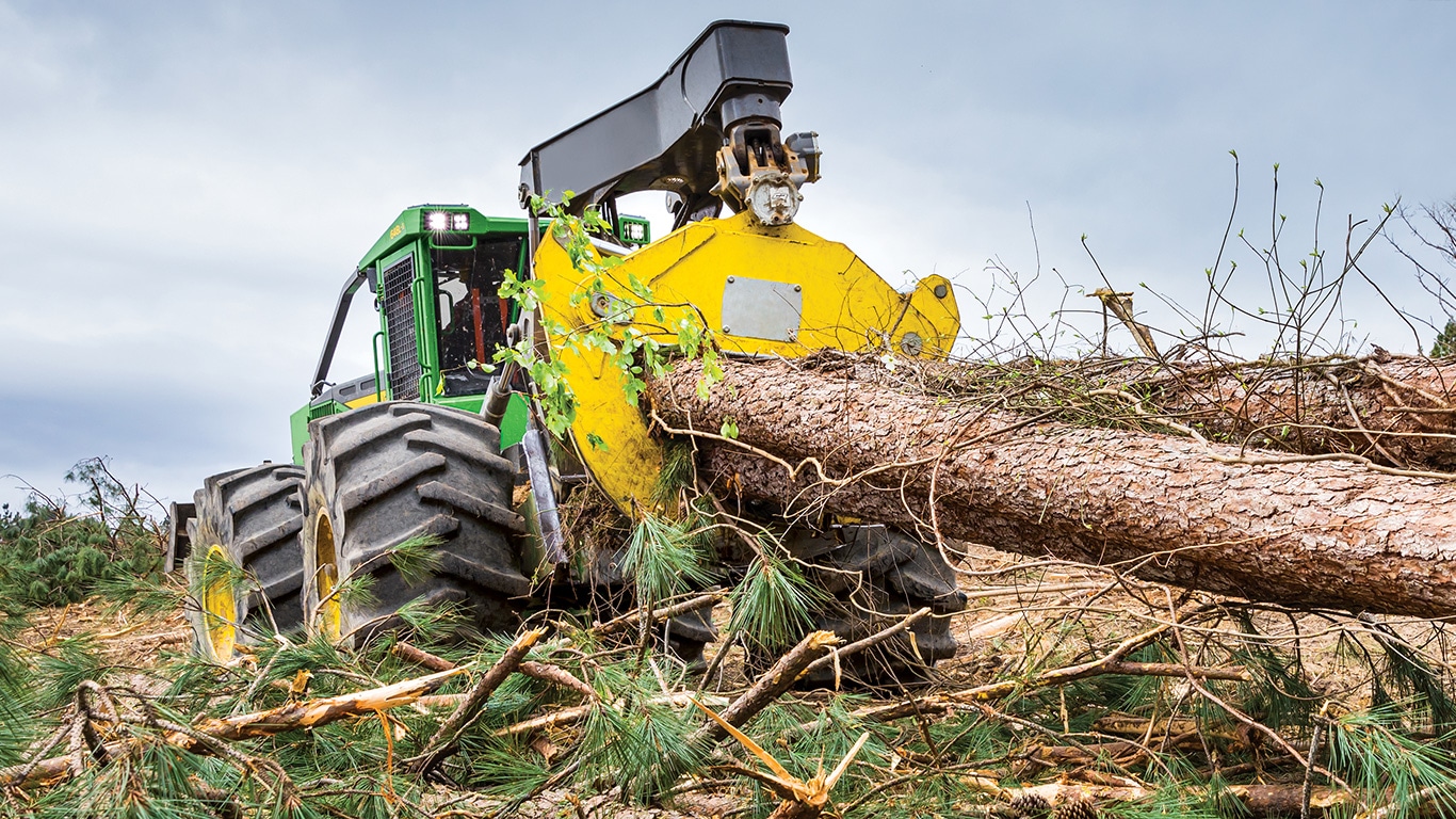 Une débardeuse à pince 648L-II John Deere traîne des rondins de la forêt vers le site de chargement.