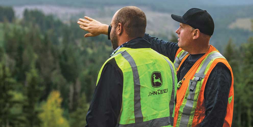 John Deere dealer and customer standing on the side of the mountain looking at the forest below