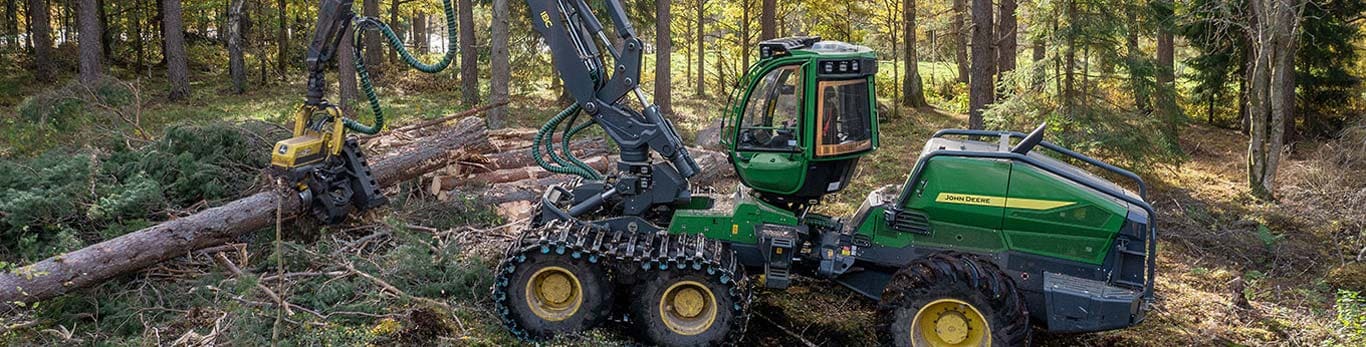 Abatteuse-façonneuse à roues John Deere qui abat des arbres dans une forêt avec sa flèche déployée.