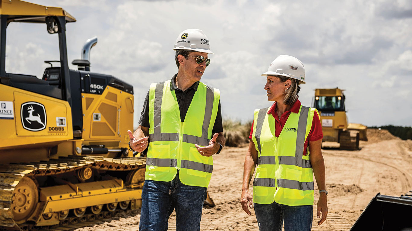 A man and woman wearing John&nbsp;Deere hard hats standing in front of a 450K dozer on a jobsite