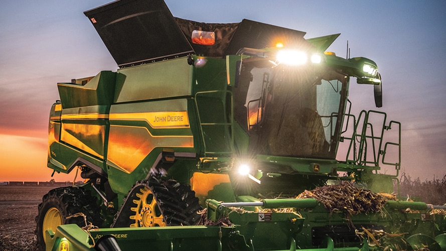 Une des nouvelles machines 9RX de John Deere avec des phares allumés au coucher du soleil