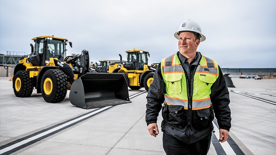 A construction worker standing at a construction site with John Deere equipment in the background