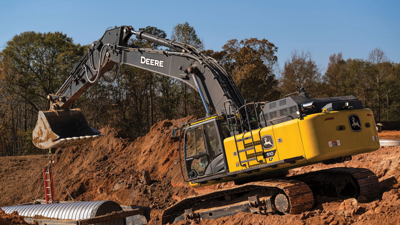 L'excavatrice 510 de catégorie P soulève une canalisation sur un chantier de construction parsemé d'amas de terre