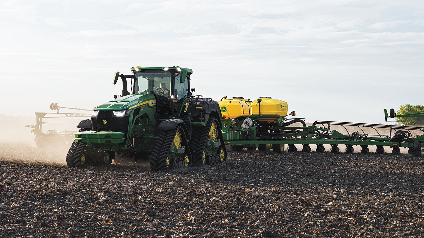 8RX tractor attached to seed planter working in a dusty field.