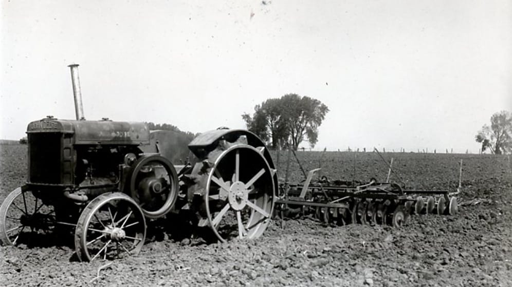early 20th century John Deere tractor tills a field in the Midwest of America