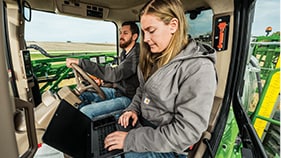 un homme et une femme dans la cabine d'un équipement John Deere