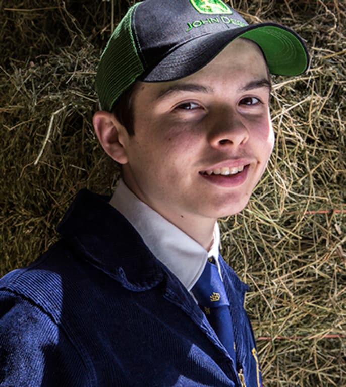 Un étudiant de la FFA portant une casquette John Deere se tient devant une balle de foin