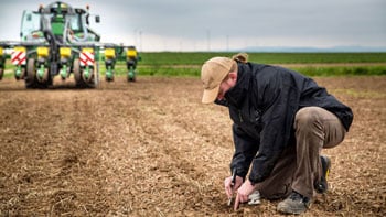 Kremmer crouched down using scraper to inspect soil with planter in background.