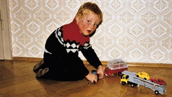 Boy plays on hardwood floor with toy trucks.