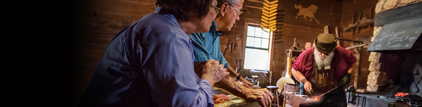 Un couple de personnes âgées observant le forgeron battre une pièce de métal au site historique de Grand Detour, dans l'Illinois, aux États-Unis.