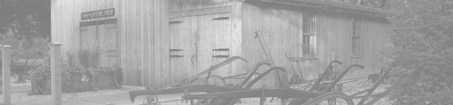 Photographie en noir et blanc tonique de la reconstitution du site historique de l’atelier de forgeron d’origine de John Deere, sur un fond vert