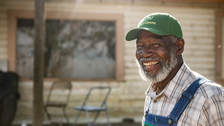Un fermier noir souriant portant un chapeau John Deere