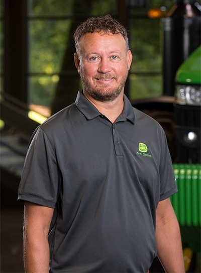 Jason Beneke stands in front of some John Deere equipment