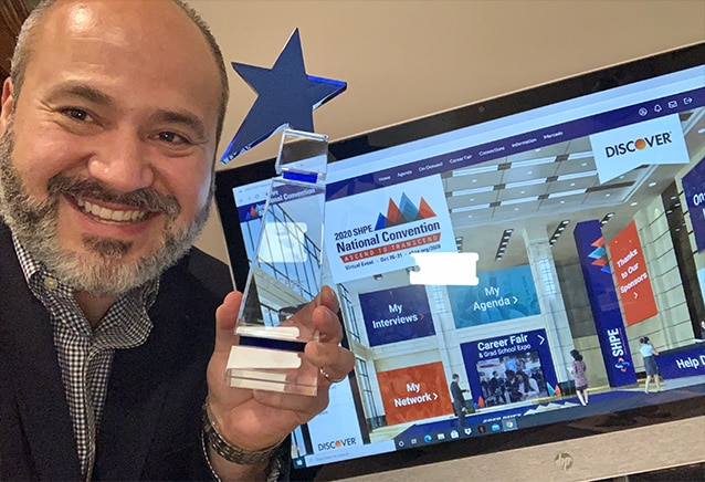 Enrique Riojas holding up his trophy at his desk