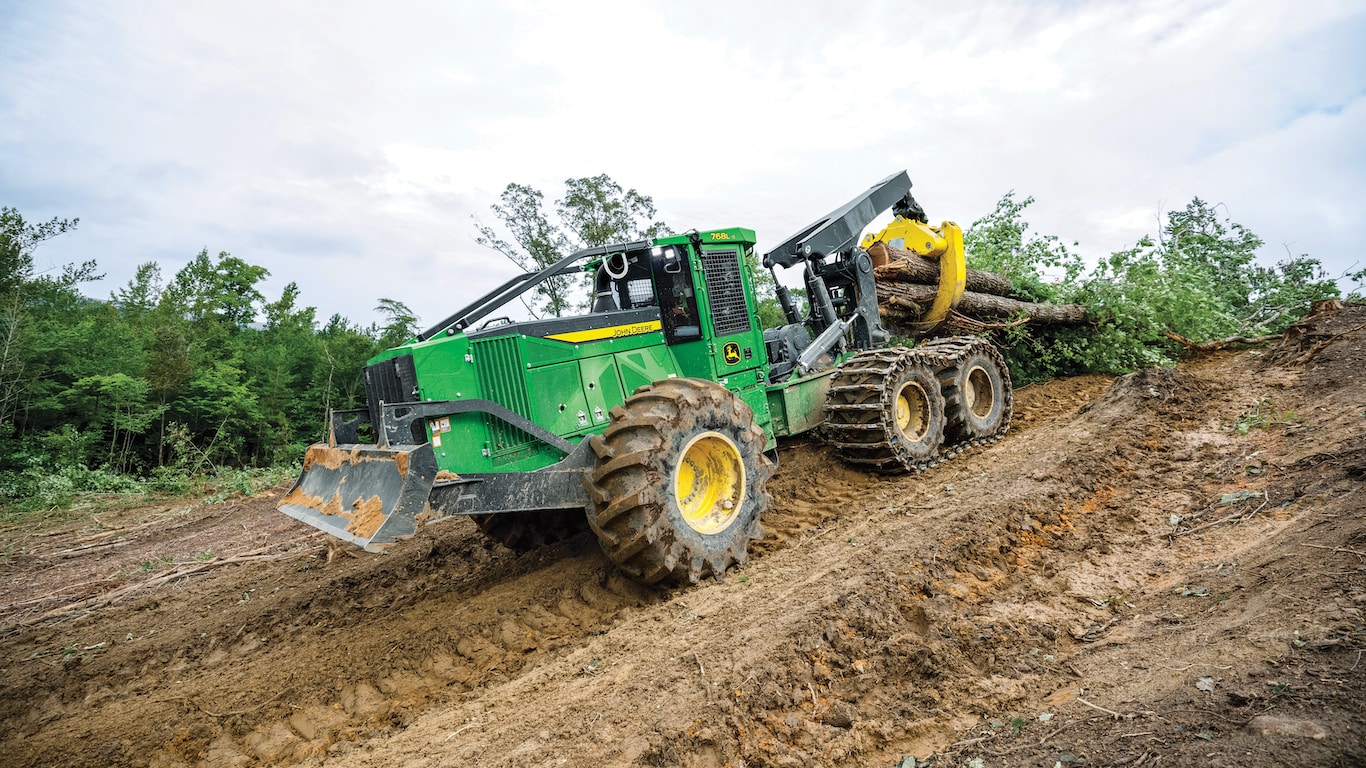 768L–II à bogies transporte une grapple pleine d'arbres abattus sur une colline en pente