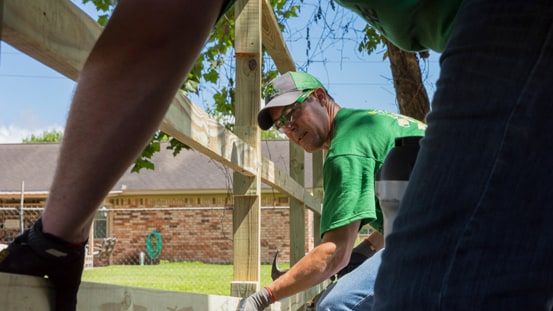 Two people building a fence together near a building.