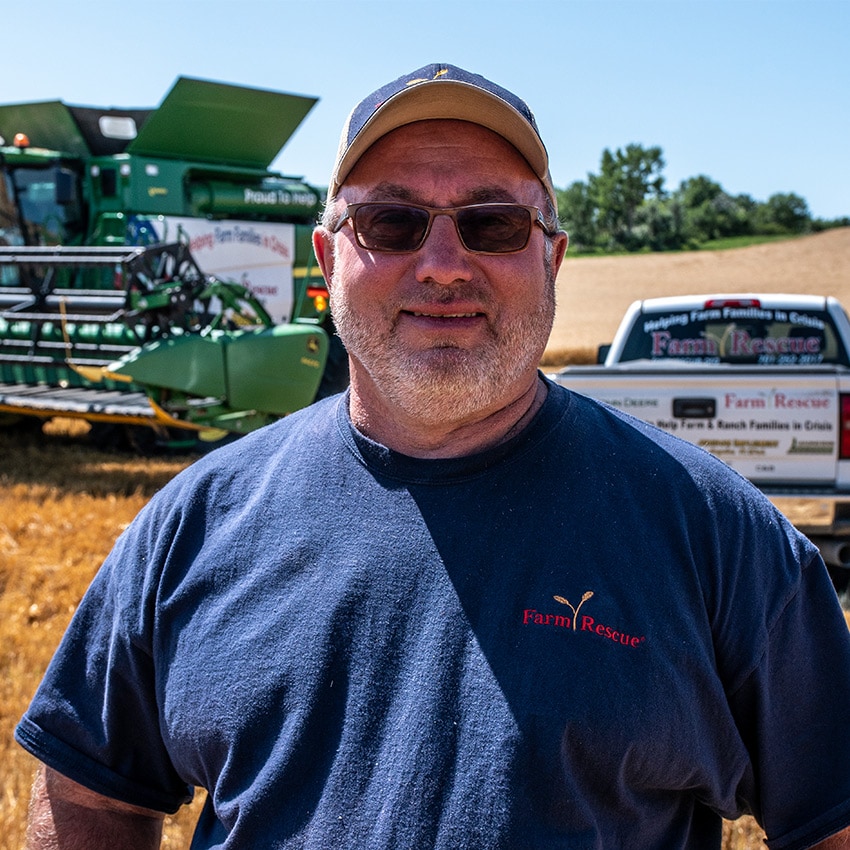 Larry Leier au premier plan avec une récolteuse John Deere à l’arrière et un camion de secours agricole.