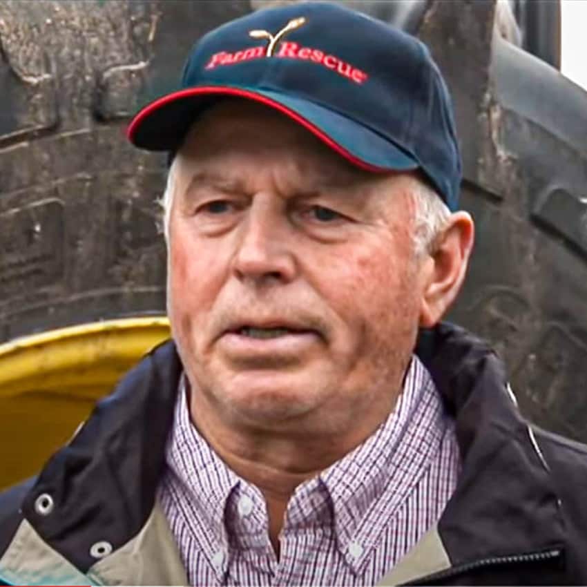 Ron Behm devant un tracteur John Deere avec un chapeau et un manteau Farm Rescue