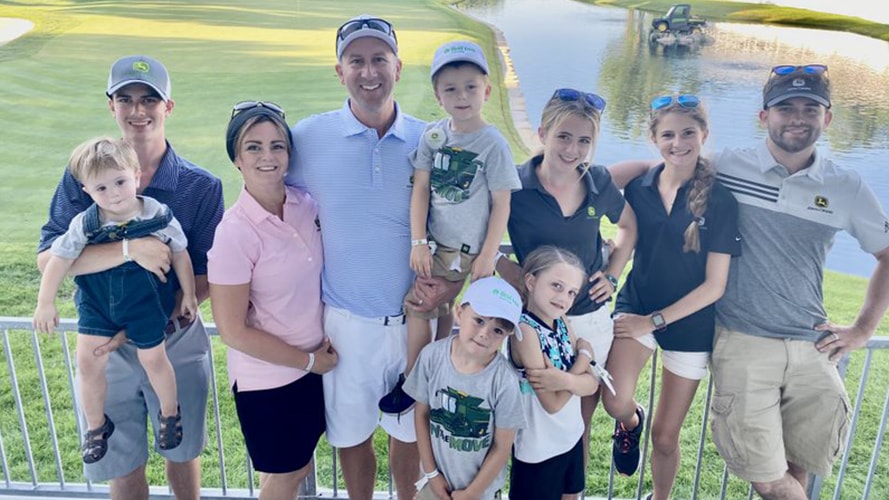 Joel Oltman with his wife and eight children smile pose together in front of the golf course 