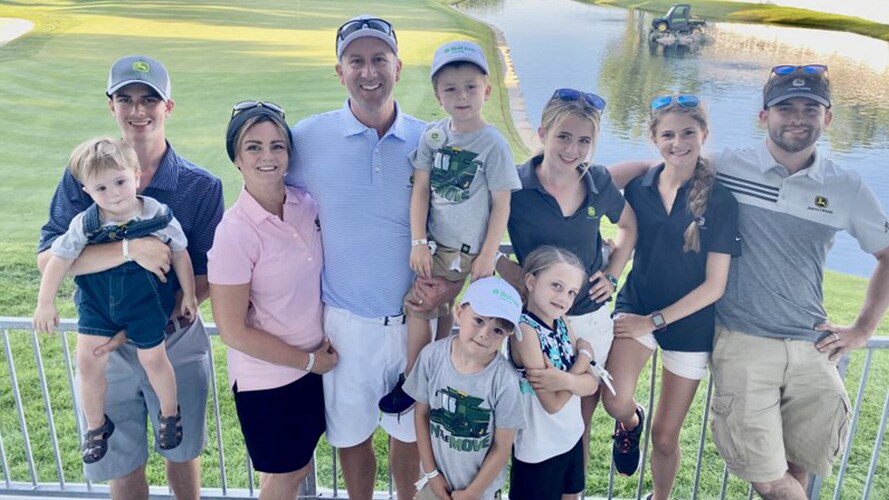 Joel Oltman with his wife and eight children smile pose together in front of the golf course