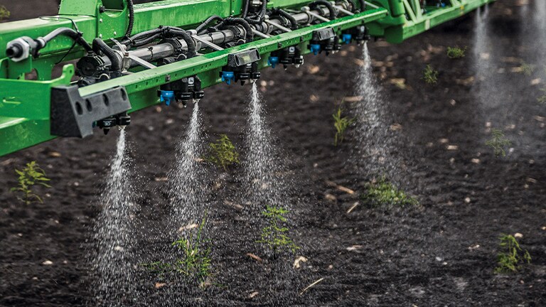 A close up view of John Deere sprayers treating plants in a field