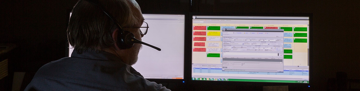 Un analyste dans une pièce faiblement éclairée examine des données sur deux écrans d’ordinateur en parlant dans un casque-micro.