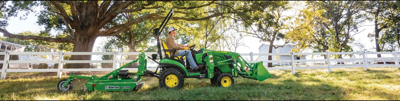 Man operates tractor with grooming mower attached to cut grass