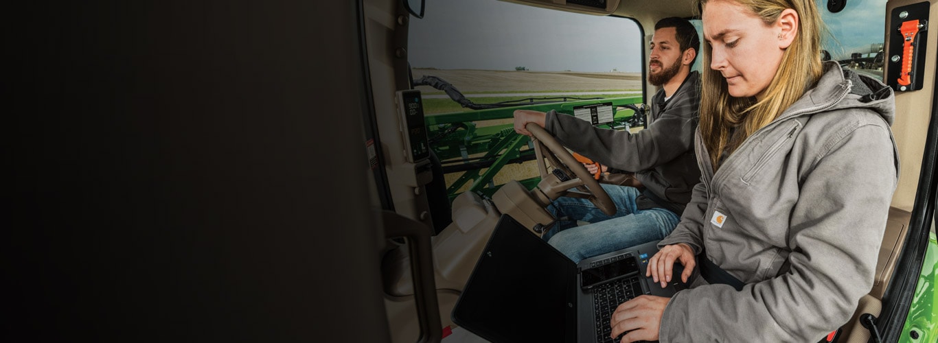 Un homme et une femme dans la cabine d'un tracteur qui utilisent, pendant leur travail, le Service ADVISOR™ pour clients.
