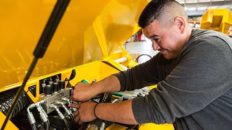 un homme travaillant sur un moteur sous un capot jaune