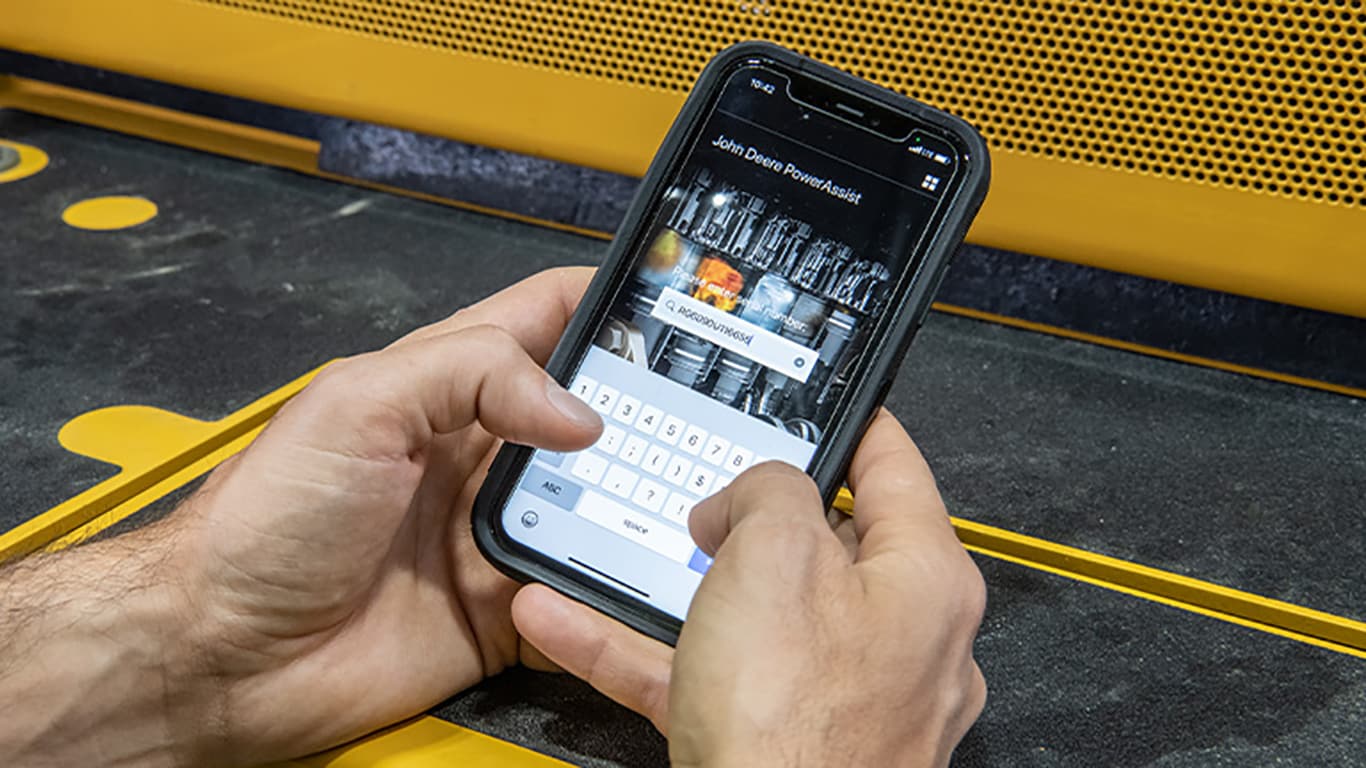 A man holding a smartphone in his hands while searching an engine serial number on the John Deere PowerAssist App