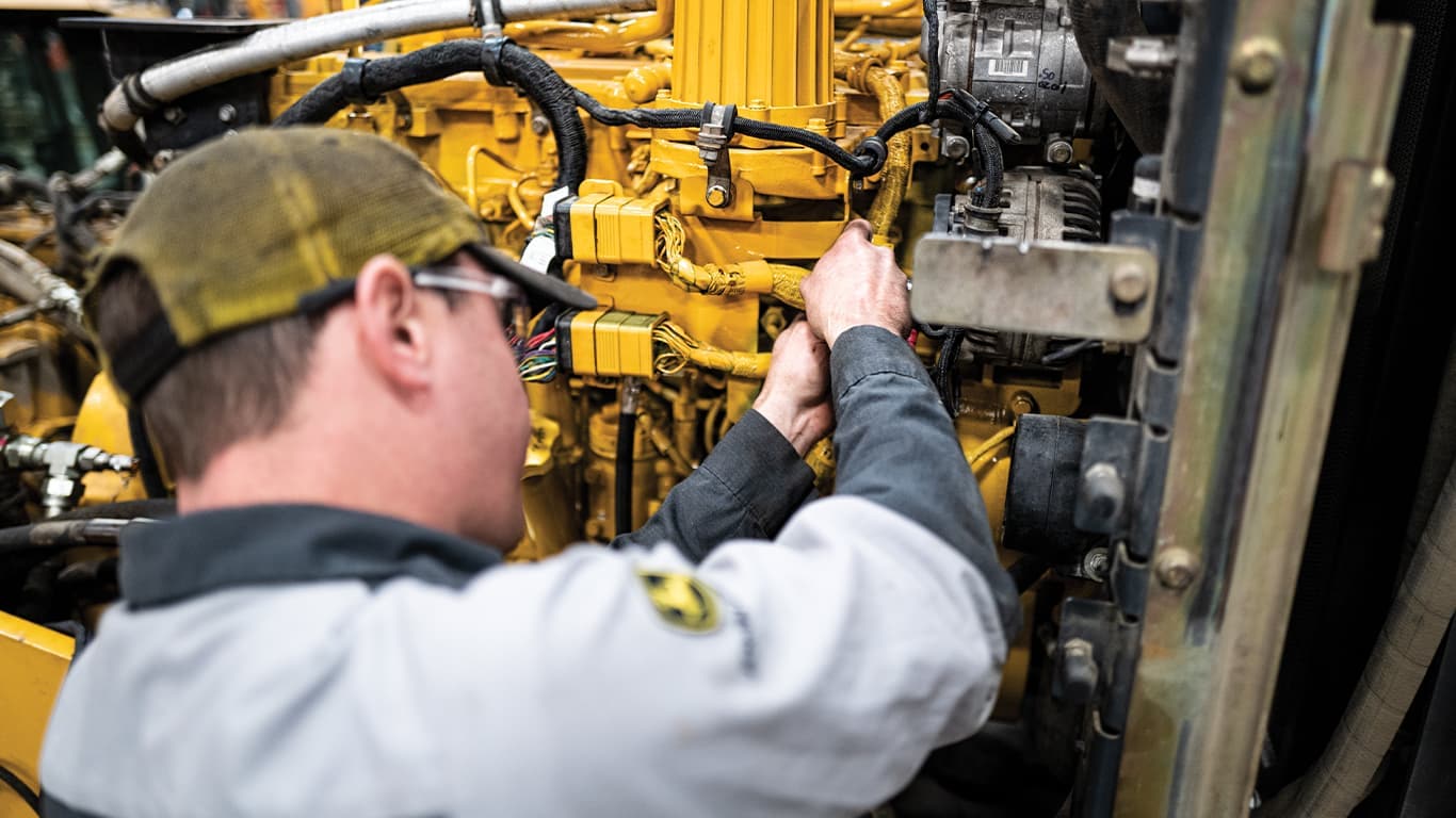 Un homme portant des lunettes de protection tout en travaillant sur un moteur John Deere