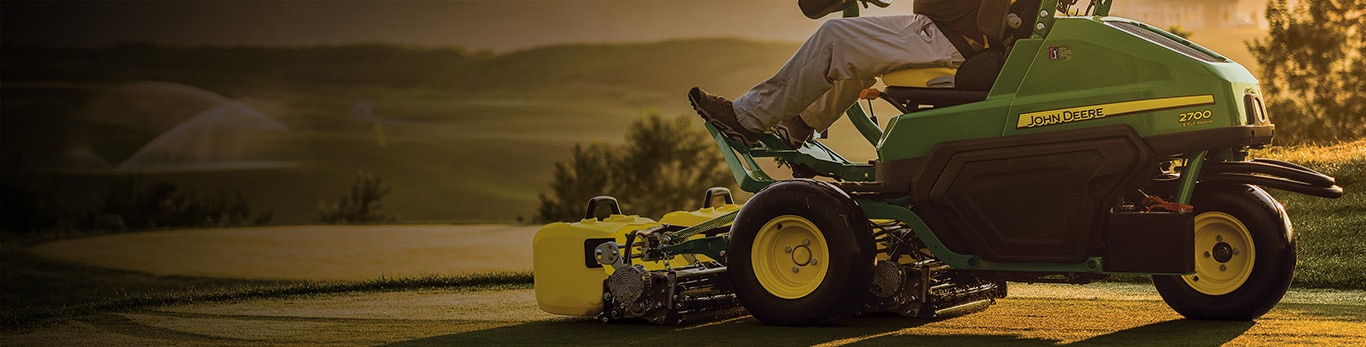 Man mowing a golf green with a riding John Deere mower.