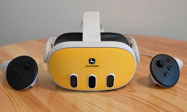 Un casque de réalité virtuelle John Deere blanc et jaune avec deux commandes posés sur une table en bois.