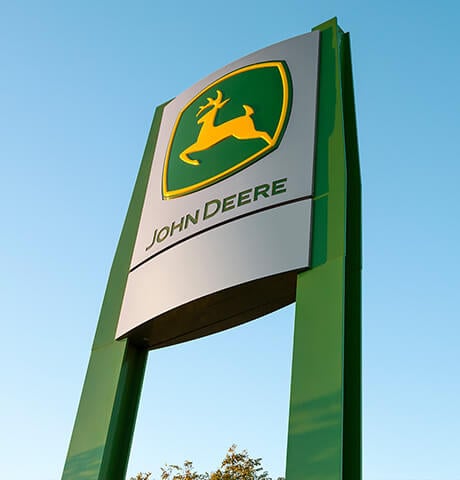 Low angle shot of a John Deere dealer sign with blue sky in the background.
