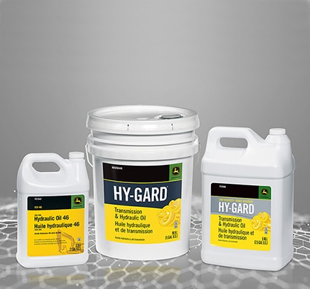 Trois récipients blancs d’huile hydraulique Deere Hy-Gard sur une surface numérisée grise.