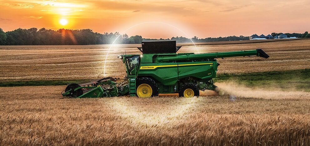 Green combine harvesting wheat in a field at sunset, leaving a trail of dust.
