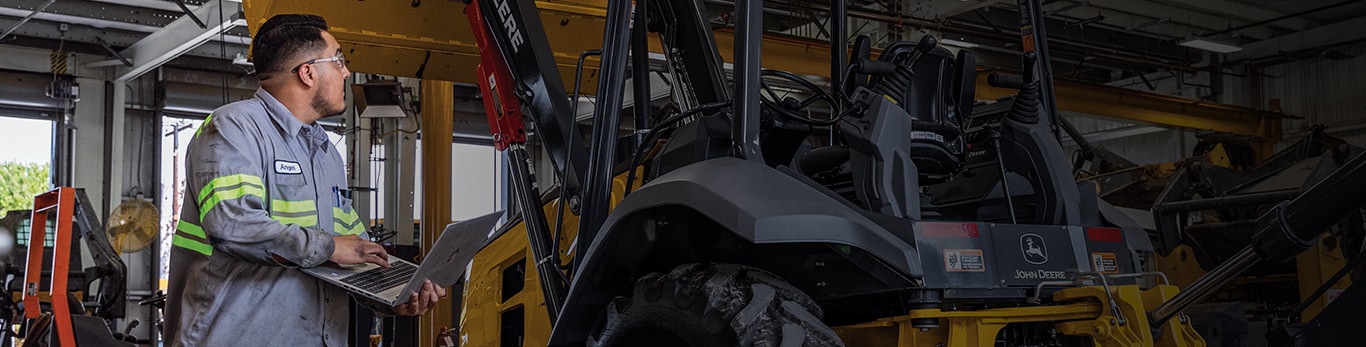 technician tracks maintenance on a laptop next to a backhoe.