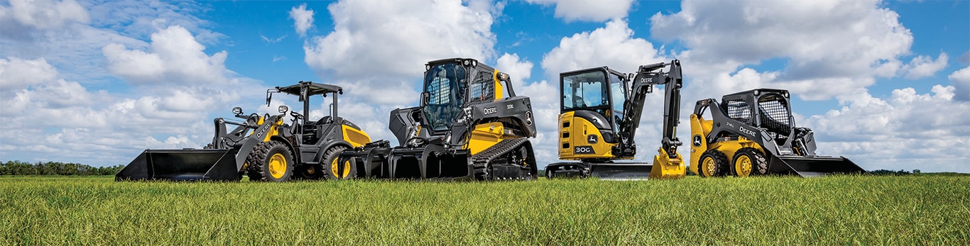 Small front end loader, tracked skid steer, mini excavator and skid steer lined up on green grassy field