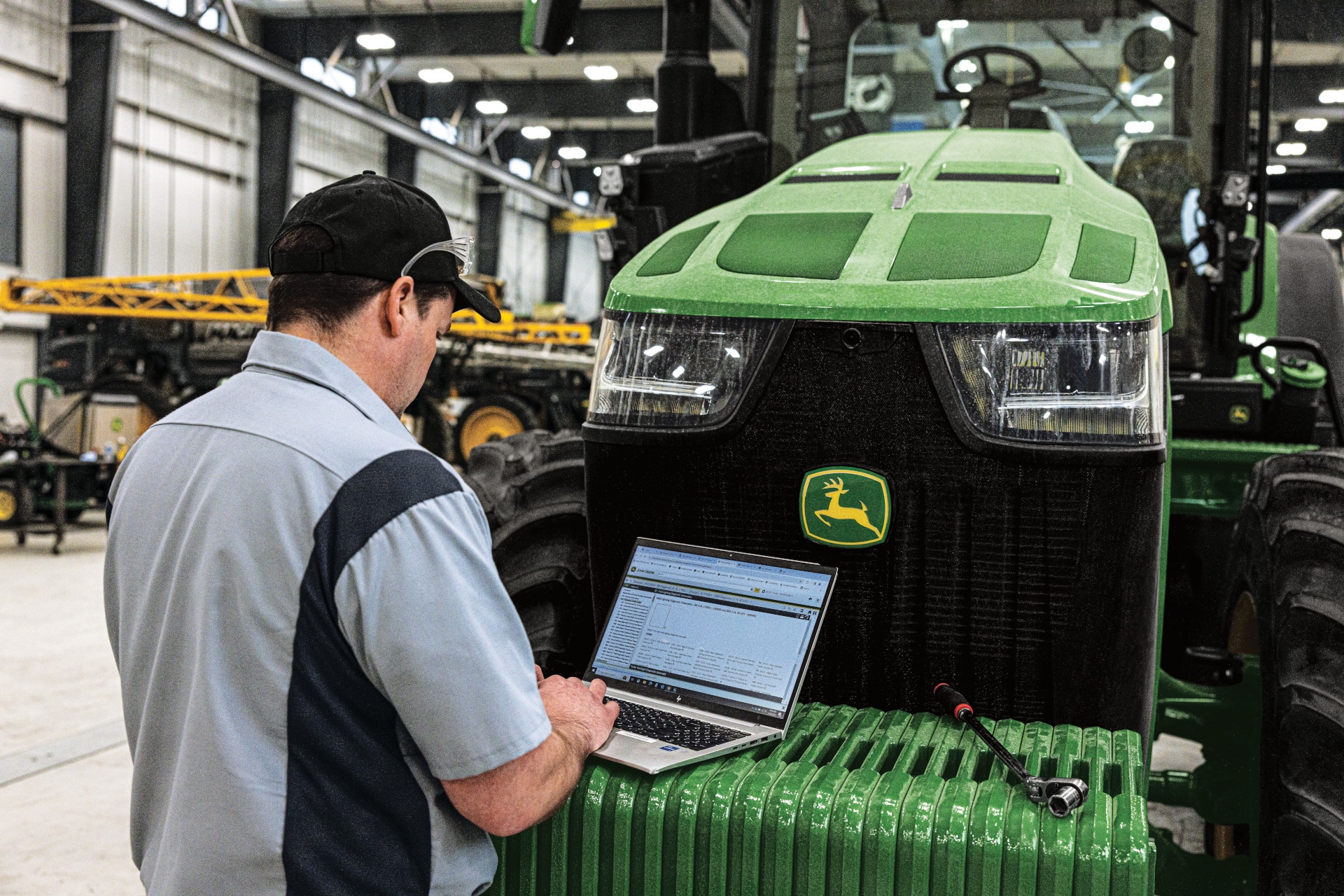 Technician using a laptop to diagnose or configure a John Deere machine inside a service facility.