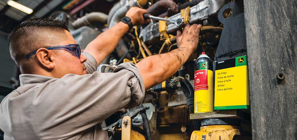 Un technicien travaille avec des fluides John Deere sur une pièce d'équipement