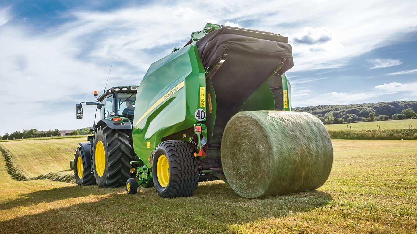 Tracteur John Deere avec rotopresse traverse un champ