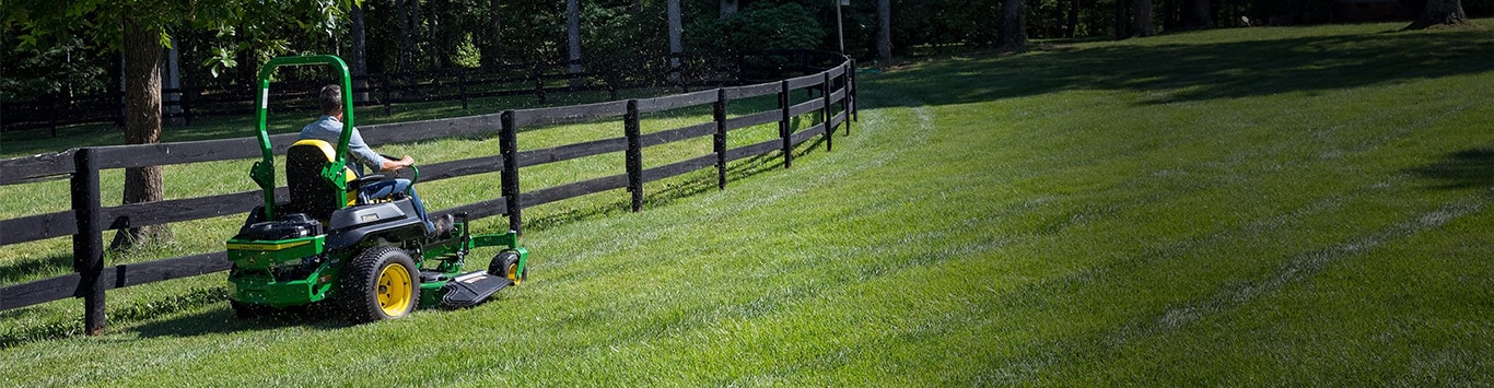 Man driving a z735m mower around a fenced pasture