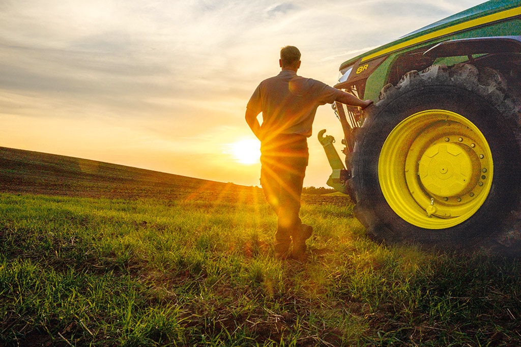 Homme debout avec son bras sur un pneu de tracteur 8R regardant vers le coucher du soleil.