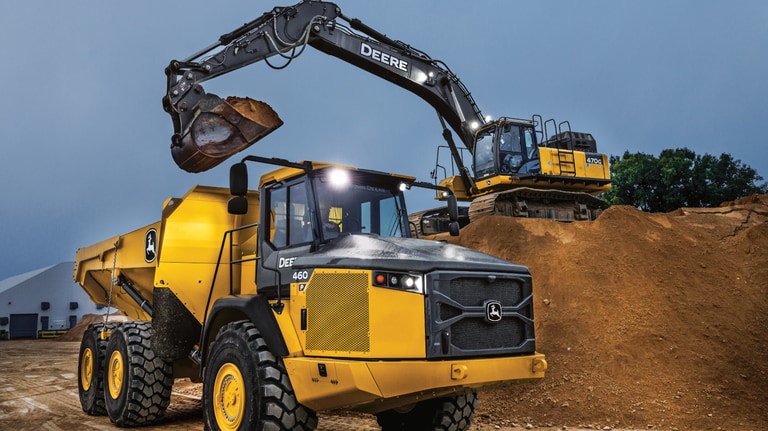 An excavator dumping dirt into a 460P Articulated Dump Truck at dusk.