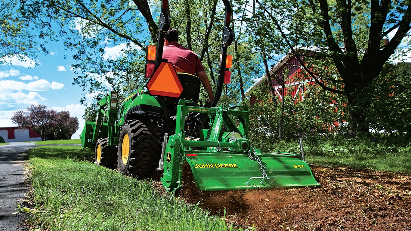Person operating a tractor with rotary tiller attachment.