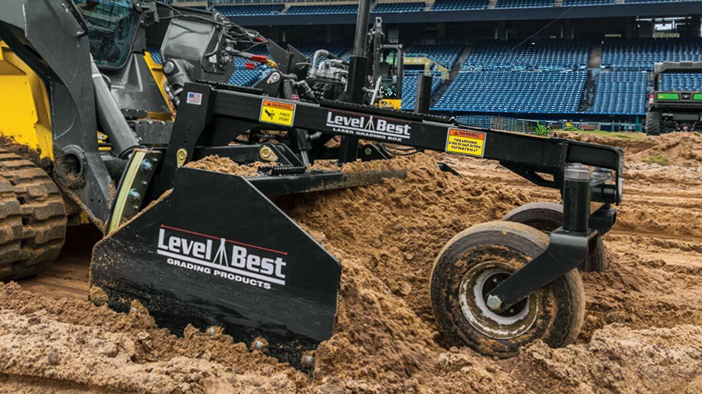 Une machine de nivellement optimale lissant les saletés sur un chantier avec des sièges de stade en arrière-plan.