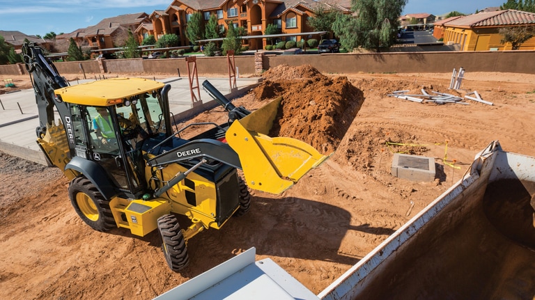 A 310G Backhoe moving dirt at a housing worksite with the house foundation in the background.