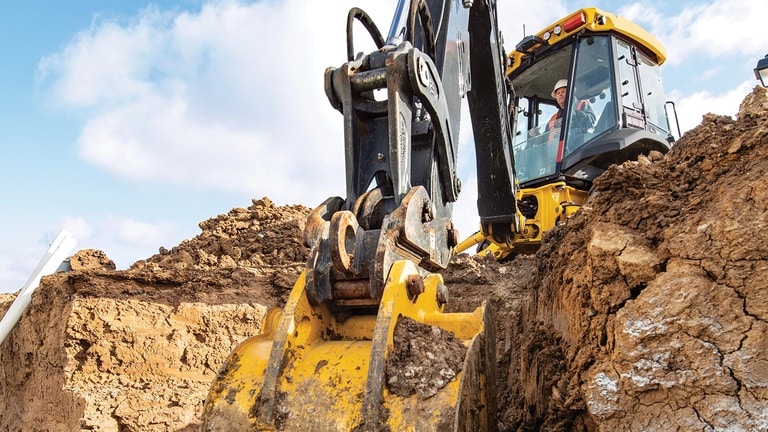 A close-up of the 320P Backhoe boom arm scooping dirt from below.